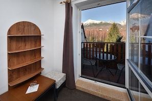 Una habitación con una estantería de madera, una mesita con vasos y vistas a un paisaje montañoso a través de un ventanal.