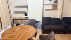 A living room with a round wooden table, a grey sofa, and a small wooden desk with a computer. - House Sleeps 2 With Parking (Croydon)