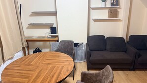 A living room with a wooden round table, two grey armchairs, a dark brown sofa, and a wooden desk with a computer and shelves. - House Sleeps 2 With Parking (Croydon)