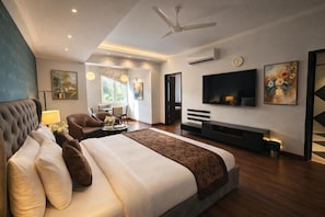 A modern hotel room with a large bed, a TV, a ceiling fan, and a seating area with a view of the outdoors. - The Solace (New Delhi)