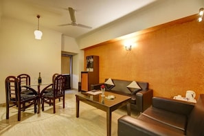 A hotel room with a dining table, chairs, a sofa, a coffee table, a ceiling fan, and a wall-mounted clock. - The Solace (New Delhi)