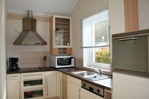 A kitchen with a microwave, oven, sink, and a window with blinds. - Bungalow Near Eifel Ski Lift (Gerolstein)