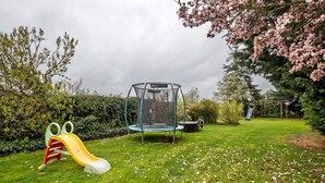 A playground with a slide and a trampoline in a grassy area with trees and bushes. - Holiday Home 'Family House with Huge Garden' with Sauna, Terrace and Wi-Fi (Jessen (Elster))