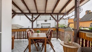 A covered patio with a wooden table and chairs, a hanging lantern, and a small table with a lantern. - Holiday Home 'Family House with Huge Garden' with Sauna, Terrace and Wi-Fi (Jessen (Elster))