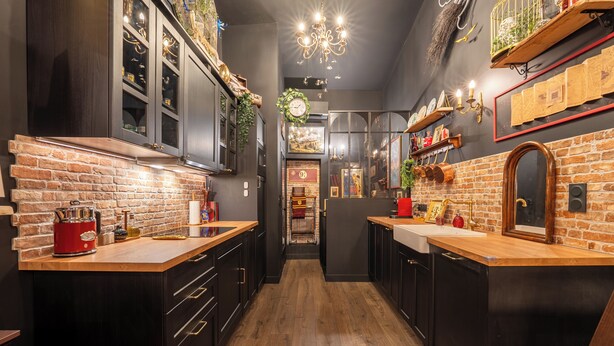 Cocina estrecha con armarios oscuros, encimeras de madera y un electrodoméstico rojo.