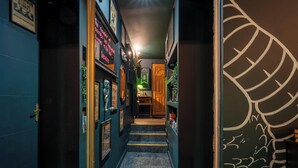 Un pasillo estrecho con cuadros en las paredes, una puerta de madera al final y un escritorio iluminado con luz verde.