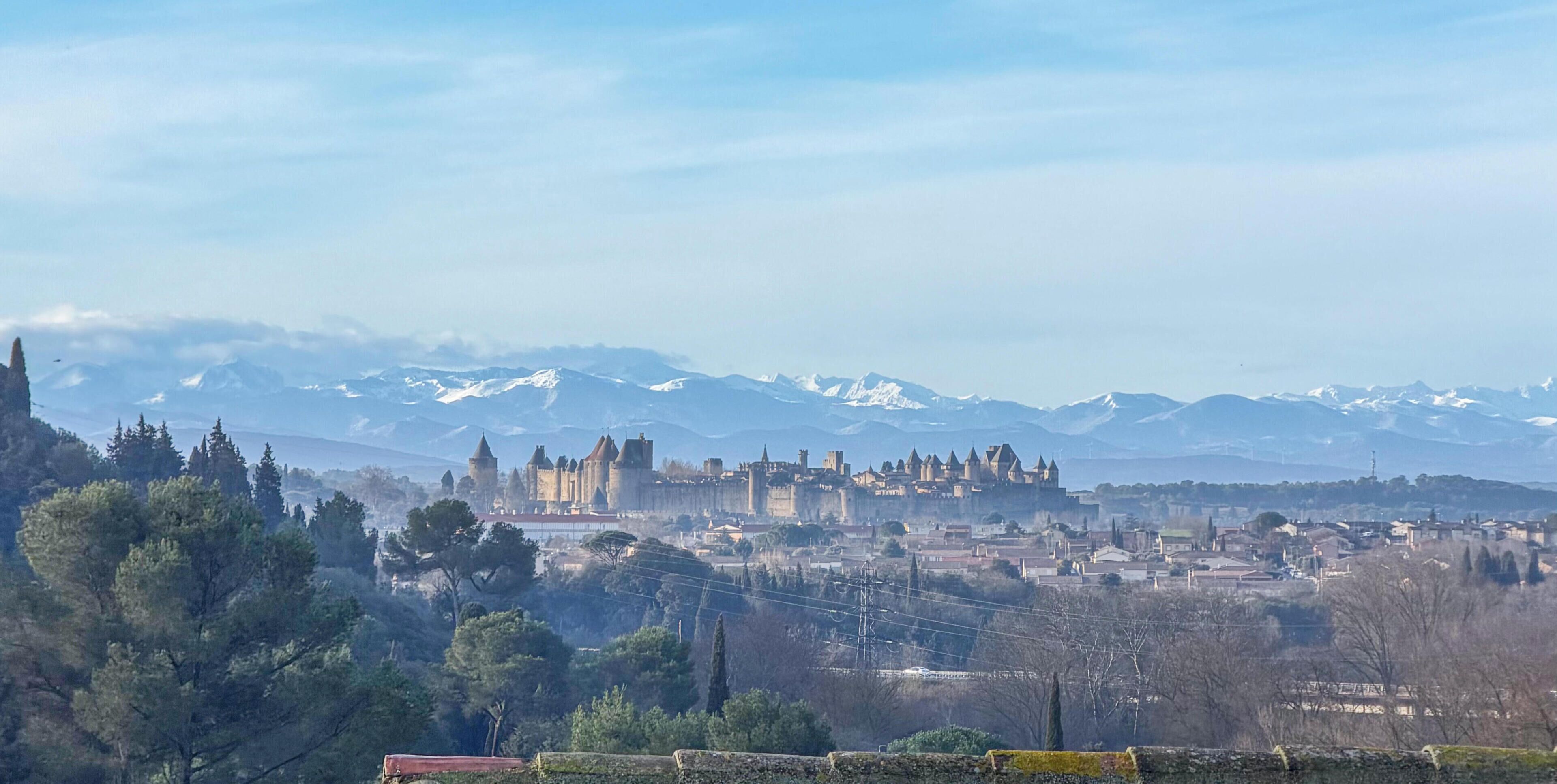 Un castello storico con numerose torri, circondato da un paese e montagne innevate sullo sfondo.