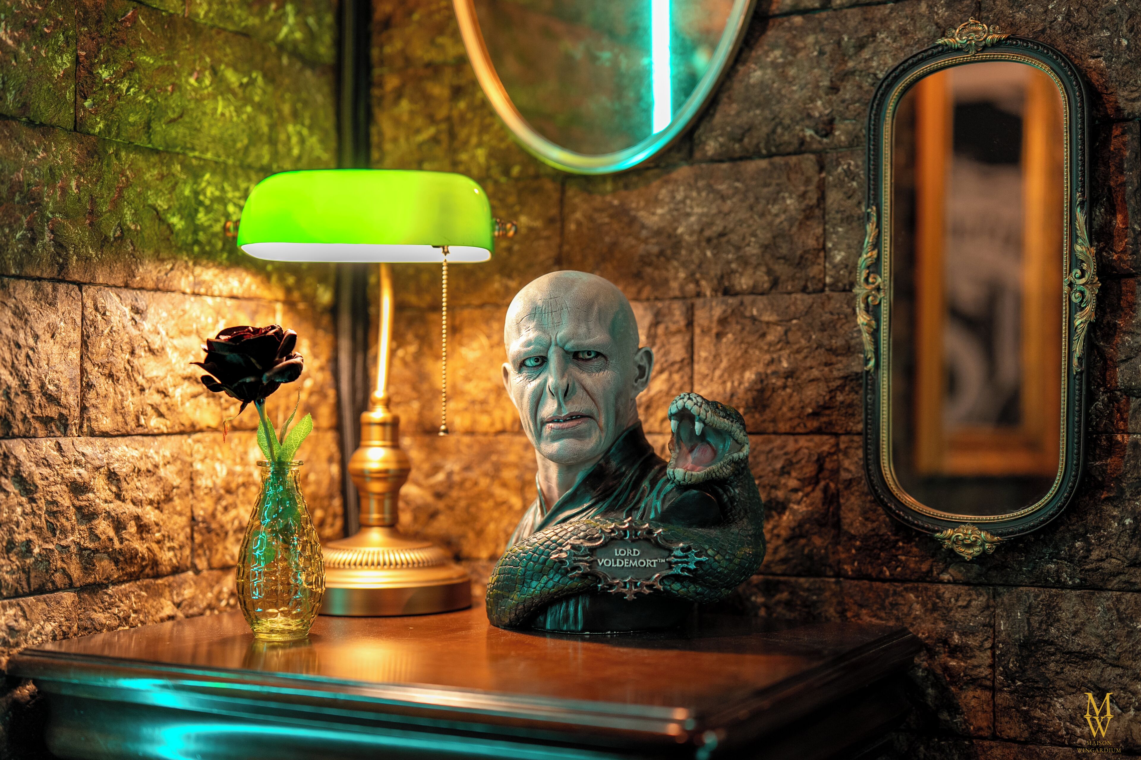 Eine Büste einer Person mit einer Schlange, eine grüne Lampe und eine Vase mit einer Rose auf einer Holzoberfläche.