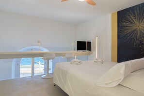 A modern hotel room with a bed, a desk with a chair, a television, and a large window overlooking the sea. - Azzurra Baveno (baveno)