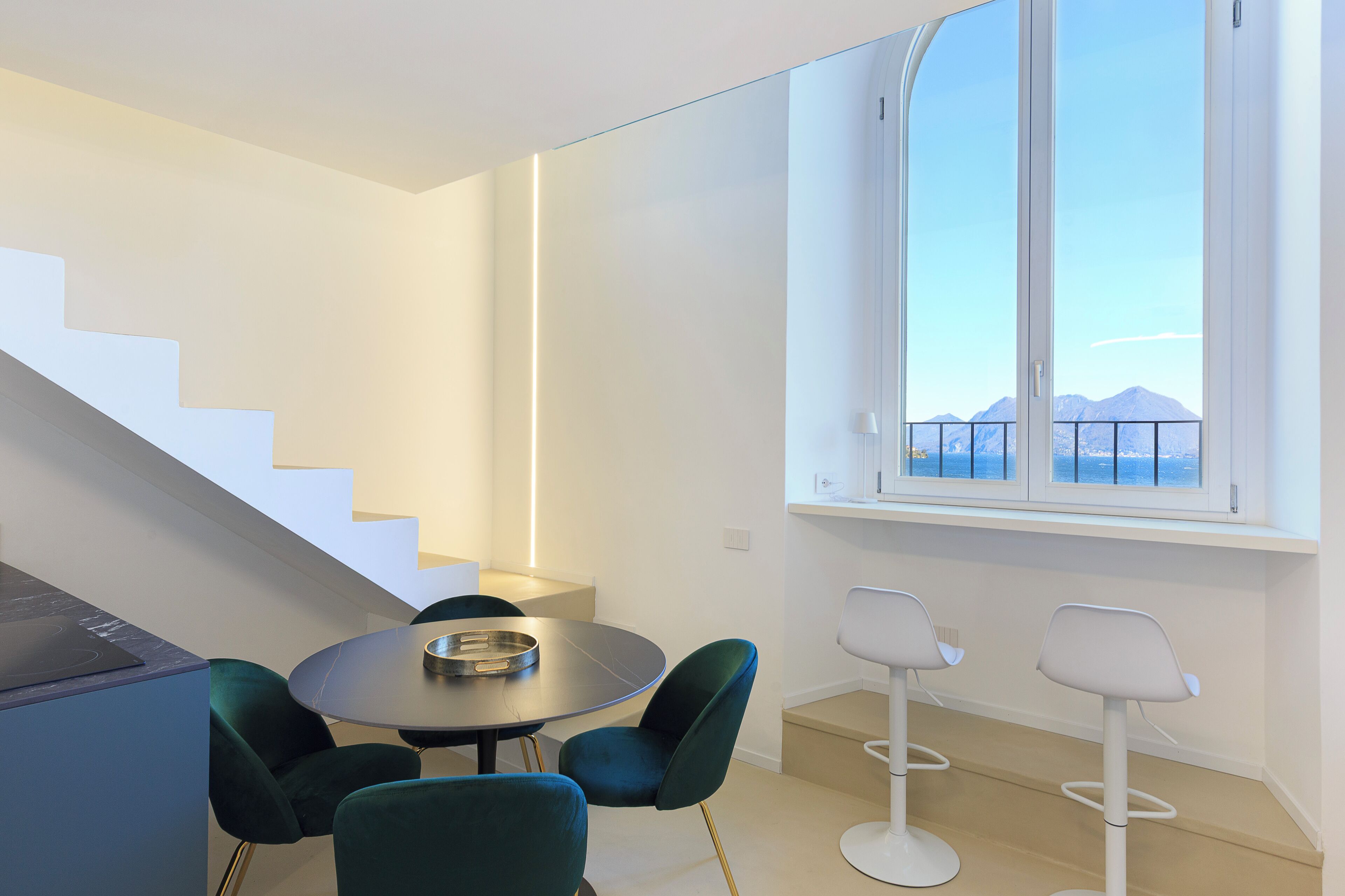 Una habitación moderna con una mesa de comedor, sillas, una escalera y un ventanal con vistas a la montaña.