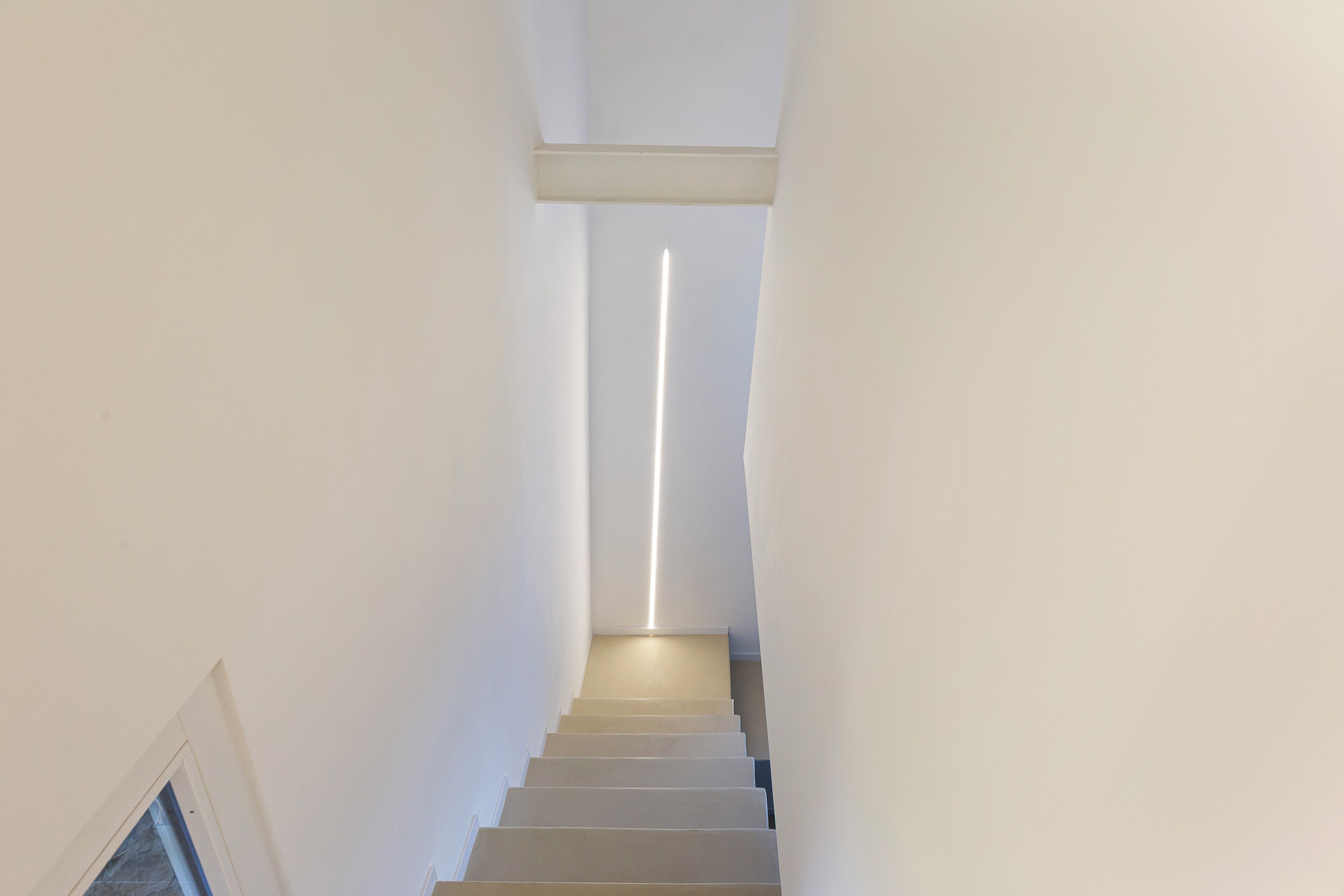 Un escalier étroit, avec une bande lumineuse qui court le long du milieu, menant à un palier.