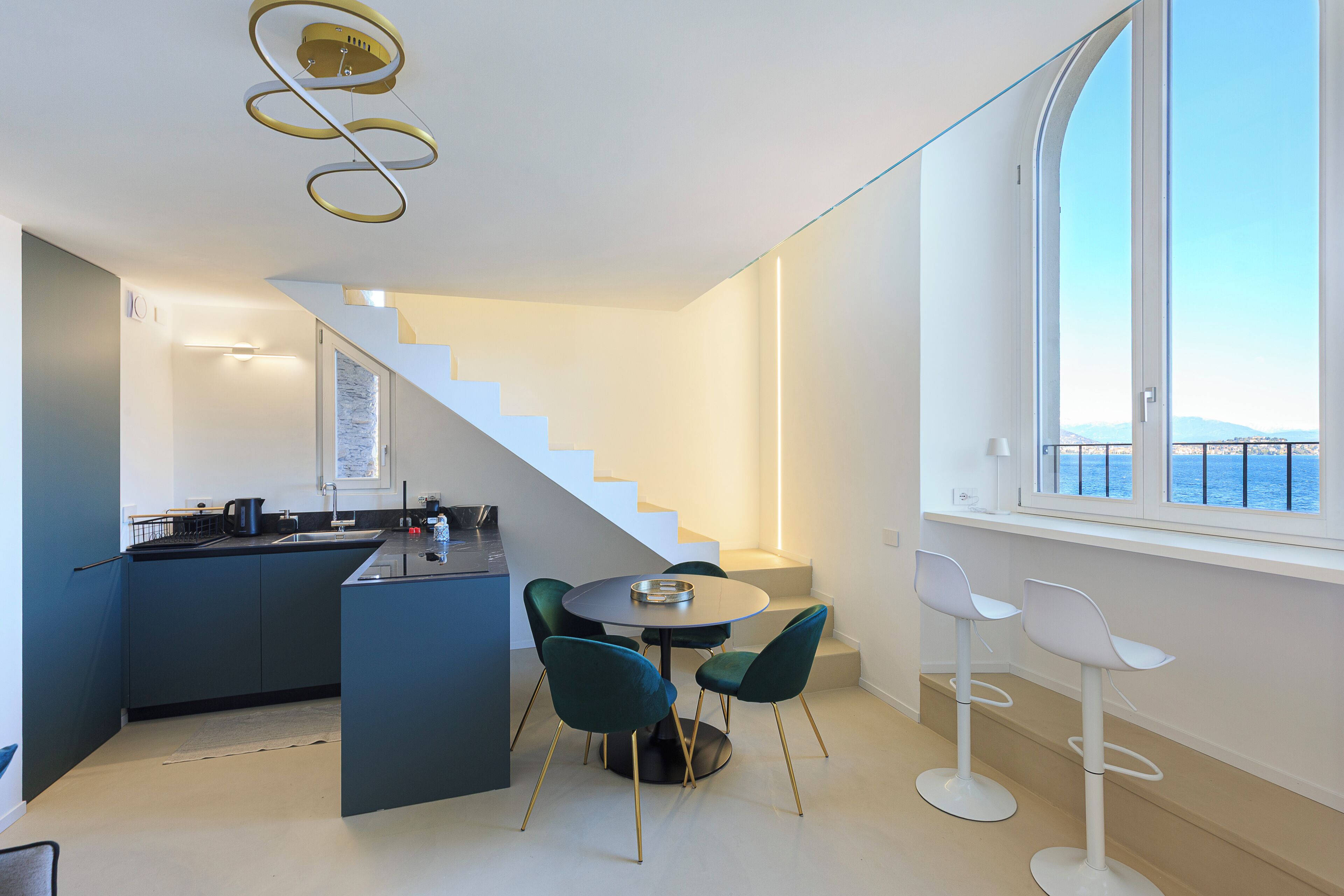 A modern kitchen with a central island, a dining area with a round table and chairs, and a staircase leading to an upper level.
