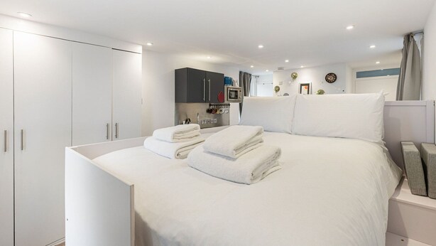 Une chambre moderne avec un grand lit, une armoire, un petit coin cuisine et une salle de bain.