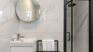 Une salle de bain moderne avec un mur en marbre, un miroir rond, un lavabo, une douche en verre et une serviette sur un porte-serviettes noir.