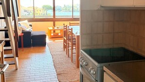 Uma cozinha com fogão, sala de jantar com cadeiras, mesa e vista para o mar através de grandes janelas.
