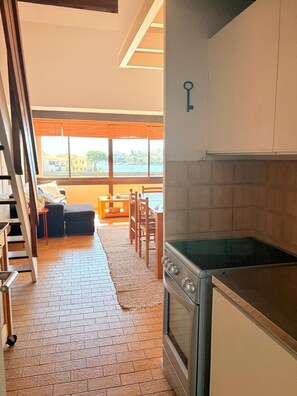 Eine Küche mit Herd, ein Essbereich mit Stühlen, einem Tisch und Blick auf das Meer durch große Fenster.