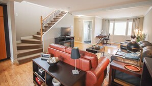 A spacious living area with a staircase, a leather sofa, a coffee table, and a television. - Inviting Townhome in St. John's City Center! (St. John's)