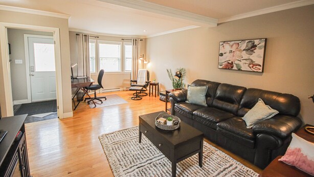 A living room with a black leather sofa, a coffee table, a desk with a chair, and a large window. - Inviting Townhome in St. John's City Center! (St. John's)