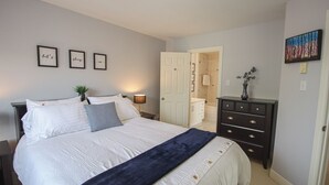 A bedroom with a bed, bedside tables, a dresser, a door leading to a bathroom, and wall art. - Inviting Townhome in St. John's City Center! (St. John's)