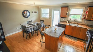 A kitchen with wooden cabinets, a dining table with chairs, a built-in island, and a window with blinds. - Inviting Townhome in St. John's City Center! (St. John's)
