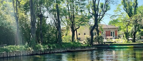 Une rivière paisible aux eaux claires, bordée d’arbres verdoyants et, au loin, un bâtiment avec un toit rouge.