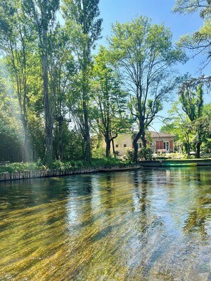 Un riu tranquil d'aigua cristal·lina, envoltat de vegetació frondosa i edifici amb teulada vermella al fons.