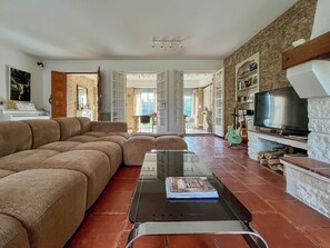 A living room with a sectional sofa, a glass coffee table, a television, and a fireplace. - Villa Alba, house with private access to the river, swimming and canoes (L'Isle-sur-la-Sorgue)