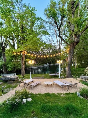 Un espace extérieur aménagé avec des tables et des chaises, entouré d’arbres et bordé par un plan d’eau.