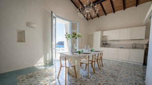 A dining area with a table set for four, a vase with flowers, and a view through an open door. - Il Cavaliere - Fantastic sea view, pool, beach only 5 minutes on foot (Lacona)