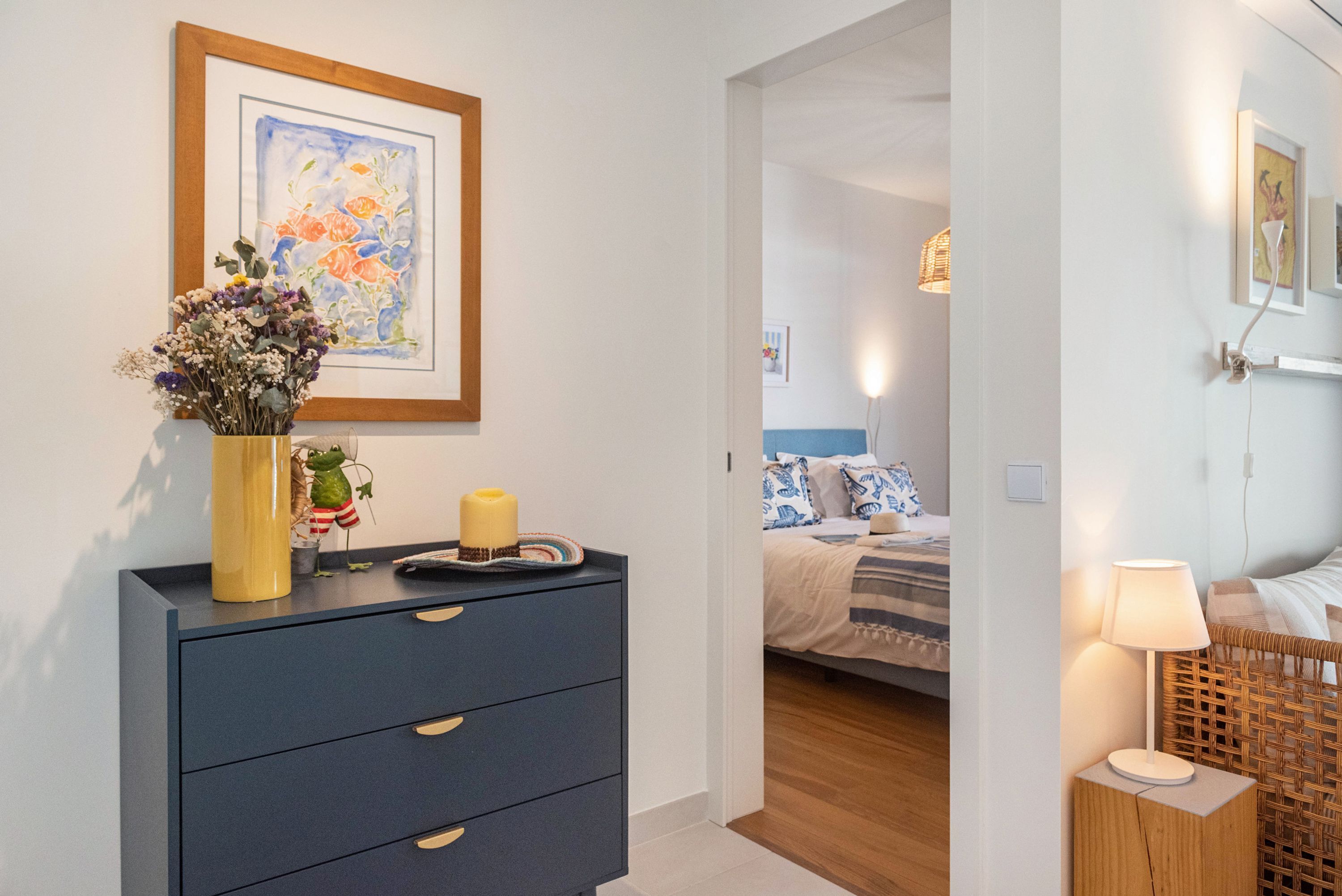 A bedroom with a bed, bedside table, lamp, and a wall-mounted painting.