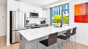 Una cucina moderna con elettrodomestici in acciaio inossidabile, un piano di lavoro bianco e un'ampia finestra con vista sul verde.
