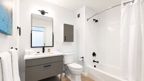 Un bagno moderno con un mobile lavabo bianco, un water, una vasca e una tenda per la doccia.