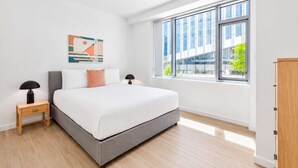 Una camera da letto moderna con un letto grande, due comodini, una finestra con vista sulla città e un'opera d'arte astratta appesa al muro.