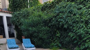 Une piscine bordée de deux chaises longues, entourée d’une terrasse carrelée et d’une végétation luxuriante.