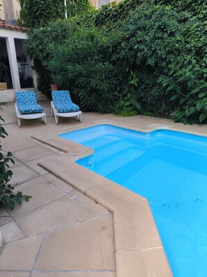 A swimming pool with two lounge chairs, surrounded by a tiled patio and dense greenery. - Art Deco apartment, swimming pool, private terrace, parking, city center (Béziers)
