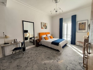 A hotel room with a bed, a desk, a chair, a mirror, a chandelier, and artwork on the walls. - Art Deco apartment, swimming pool, private terrace, parking, city center (Béziers)