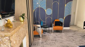 Une chambre d’hôtel avec une télévision, une plante, une petite table, deux chaises et un sol à motifs.