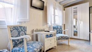 Een kamer met twee stoelen, een kleine witte dressoir, een aan de muur bevestigde televisie en een garderobe.