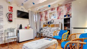 Een woonkamer met een televisie, een brandblusser, een koffiezetapparaat, rieten meubels en een krantenrek.