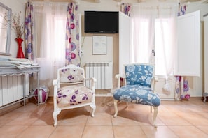 Una habitación con dos sillas, un radiador, un televisor y una ventana con cortinas.