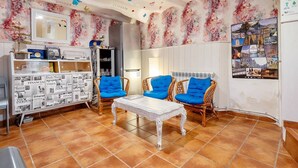 Een kamer met een witte salontafel, blauwe stoelen, een witte kast met kranten en bloemenbehang.