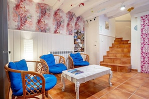 Una sala de estar con sillones de mimbre, una mesa de centro blanca, una escalera y un diseño floral en la pared.