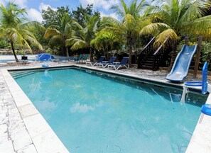 A swimming pool with lounge chairs and a slide, surrounded by palm trees. - Cozy home/Pool/Volleyball court/ near the beach (Providenciales)