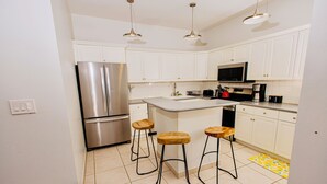 A modern kitchen with white cabinets, stainless steel appliances, wooden stools, and pendant lighting. - Cozy home/Pool/Volleyball court/ near the beach (Providenciales)