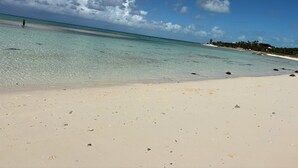 A beach with clear turquoise water, white sand, and scattered rocks. - Cozy home/Pool/Volleyball court/ near the beach (Providenciales)