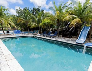 Ein Swimmingpool mit Liegestühlen und einer Rutsche, umgeben von Palmen.