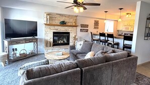 A living room with a fireplace, a sofa, a TV, and a ceiling fan. - Stunning Lake Views at Indian Pointe! (Osage Beach)