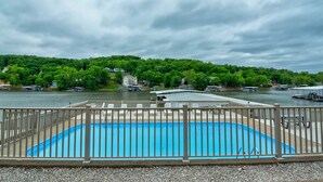 A swimming pool with a wooden deck and a view of a river and forested area. - Stunning Lake Views at Indian Pointe! (Osage Beach)