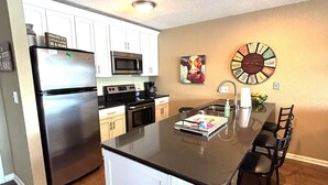 A modern kitchen with white cabinets, stainless steel appliances, and a central island with bar stools. - Beautiful Views at Bay Point Condominiums! (Osage Township)