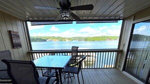 A covered deck with a table and chairs, a ceiling fan, and a view of a lake. - Beautiful Views at Bay Point Condominiums! (Osage Township)